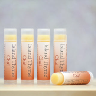 Four upright tubes and one horizontal tube of Chai Lip Balm are displayed on a light surface, set against a softly blurred background.