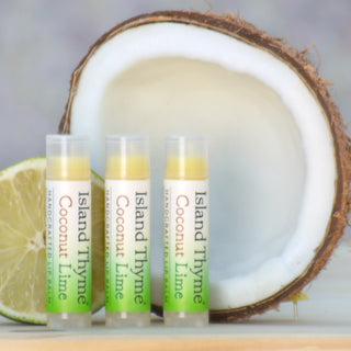 Three Coconut Lime Lip Balm tubes are shown in front of a halved coconut and a lime slice, with a blurred background.