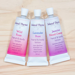 The Floral Travel Lotion Trio, featuring Wild Rose, Lavender, and Jasmine Blood Orange lotions in gradient pink and white biodegradable tubes, is displayed side by side on a light wooden surface.