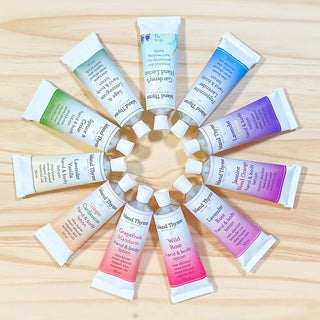 Twelve tubes from the Travel Lotion Complete Set, each Island Thyme scented and travel-sized, are arranged on a light wooden surface in a circular, flower-like pattern with each tube facing outward.