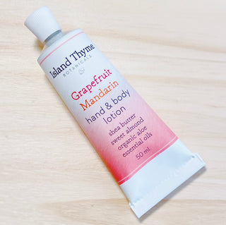 A tube of Grapefruit Mandarin Lotion by Island Thyme Botanicals, enriched with shea butter, sweet almond oil, organic aloe, and essential oils, sits on a light wooden surface.