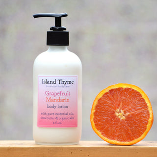 A bottle of Grapefruit Mandarin Lotion in Eco Size with a pump sits beside a fresh grapefruit slice on a wooden surface, emphasizing its refreshing citrus scent against a softly blurred background.