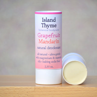 A tube of Grapefruit Mandarin Deodorant sits with its cap off, revealing the pale solid inside. The biodegradable paper tube’s label notes it is baking soda free and made with essential oils.