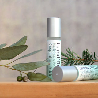 Two Eucalyptus & Fir Respiratory Stick tubes are displayed on a wooden surface, accented with eucalyptus leaves and pine sprigs in the background.
