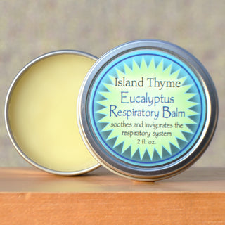 A round, open metal tin of Eucalyptus Respiratory Balm sits on wood. The label says: soothes and invigorates the respiratory system, provides natural sinus soother and chest congestion relief, 2 fl. oz.