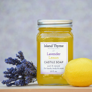 A jar of Lavender Lemon Castile Soap is shown with fresh lavender and a lemon, set against a softly blurred background.
