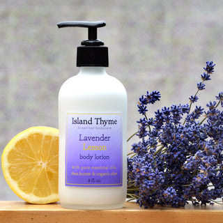 A bottle of Lavender Lemon Lotion stands on a surface beside a halved lemon and fresh lavender flowers, set against a softly blurred background.