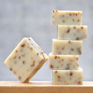 Six beige bars of Orcas Lavender Soap with brown specks, crafted from natural ingredients, are stacked on wood; five form a vertical pile and one leans diagonally, their simple elegance highlighted by a neutral, blurred background.