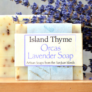A bar of Orcas Lavender Soap, crafted with natural ingredients, rests before dried lavender flowers. The label reads: Orcas Lavender Soap, Artisan Soaps from the San Juan Islands.