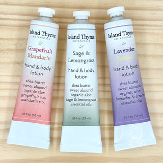 The Gift - Citrus Travel Lotion Trio features three travel-sized lotions—Grapefruit Mandarin, Sage & Lemongrass, and Lavender Lemon—arranged on a light wooden surface, making a perfect gift or convenient way to enjoy your favorite scents anywhere.