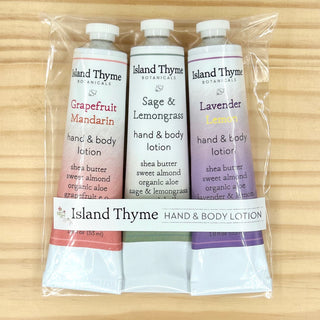 The Gift - Citrus Travel Lotion Trio, featuring three travel-sized lotions in a clear bag with Grapefruit Mandarin, Sage & Lemongrass, and Lavender scents, makes an ideal gift set on a light wooden surface.