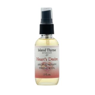 A clear glass bottle labeled Heart's Desire Aromatherapy Massage Oil, 2 fl. oz., with a black spray cap and light yellow oil, contains pure essential oils as a natural moisturizer and is shown against a white background.
