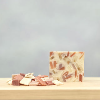 Confetti Soap—with embedded colorful fragments made from recycled soap bits—rests on a wooden surface beside similar pieces, set against a plain light gray background that highlights its creative, eco-friendly design.