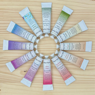Twelve tubes from the Travel Lotion Complete Set, featuring Island Thyme scents, are arranged in a circle on a wooden surface with their openings forming the center like a flower.