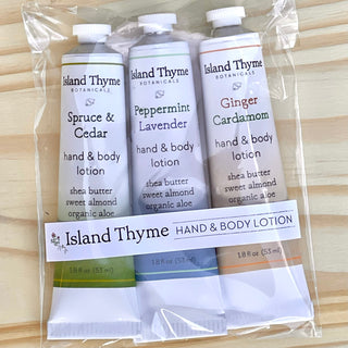 The Holiday Travel Lotion Trio features three travel-sized moisturizers—Spruce & Cedar, Peppermint Lavender, and Ginger Cardamom—in a clear bag, creating a forest-scented gift set displayed on a light wooden surface.