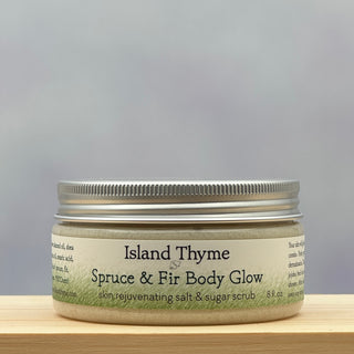 An 8 oz jar of Spruce & Fir Body Glow Salt & Sugar Scrub, a rejuvenating exfoliating body scrub, sits on a wooden surface with a soft, blurred gradient background.