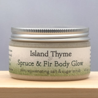 A 4 fl oz jar of Spruce & Fir Body Glow Salt & Sugar Scrub sits on a wooden surface against a light gray background.