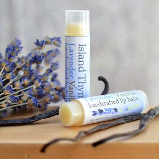 Two tubes of Lavender Vanilla Lip Balm rest on a wooden surface, accompanied by dried lavender sprigs and vanilla beans for decoration.