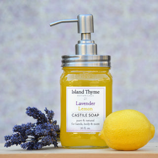 A pump dispenser jar of Lavender Lemon Castile Soap sits on a surface, accompanied by a lemon and lavender flowers, with a soft, blurred background.