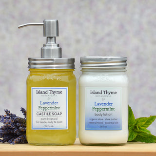 The Lavender Peppermint Lotion + Soap Set features lotion with a silver lid and castile soap with a pump, beautifully accented by fresh mint leaves and lavender sprigs.