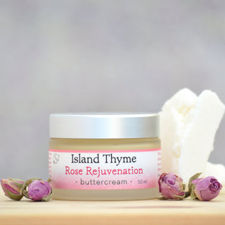 Rose Rejuvenation Buttercream is displayed on a wooden surface, accompanied by dried rosebuds and shea butter, set against a soft, neutral background.