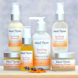 Six Island Thyme Botanicals Soothing Flowers Daily Moisturizer, enriched with coQ10 and sea buckthorn, is displayed on a light wooden surface with dried flower petals in front and a softly blurred background.