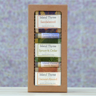 The Earthy Gift Box features five Island Thyme handcrafted soaps in assorted scents—including Spruce & Cedar—against a soft purple background. Pair with our scented lip balms for a thoughtful gift.
