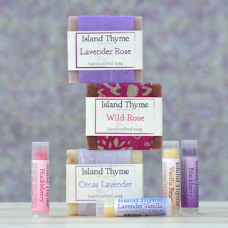 The Floral Gift Box includes three handcrafted Island Thyme soaps—Lavender Rose, Wild Rose, and Orcas Lavender—and five scented lip balms, artfully arranged on a light background with soft purple and floral accents.
