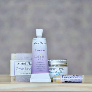 The Lavender Gift Set from Island Thyme Botanicals includes hand and body lotion, handcrafted soap, soothing skin salve, and a lavender vanilla lip balm, all arranged neatly against a neutral background.