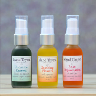 The Serum Trio by Island Thyme Botanicals, featuring Cucumber Renewal, Soothing Flowers, and Rose Rejuvenation serums, is arranged on a wooden surface—ideal for boosting your skincare routine with hydrated, glowing results.